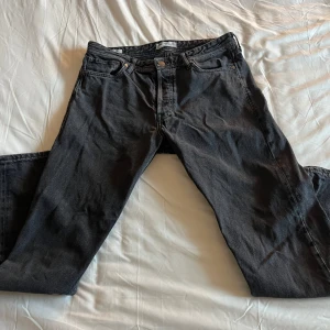 Svarta jeansbyxor - Säljer ett par svarta jeansbyxor med normal passform. De har en klassisk design med dragkedja och knappar. Perfekta för en avslappnad stil. Storlek 32W 32L