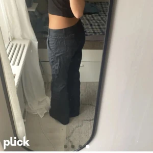 Svarta cargopants - Säljer ett par svarta cargopants med låg midja och bootcut-stil. Byxorna har flera fickor och en knappdetalj framtill. Perfekta för en avslappnad look.