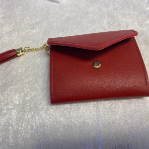 Tredubbel Dam plånböcker med tofs och hjärtdetalj - Säljer flera stilrena plånböcker i olika färger: röd, grön, grå och svart. Varje plånbok har en elegant tofs och en hjärtdetalj i guld. Perfekt för att hålla ordning på kort och kontanter med stil.  Helt ny , 85kr/st 