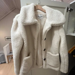 Vit teddyjacka från NA-KD - Mysig vit teddyjacka från NA-KD med stora knappar och två fickor framtill. Perfekt för kyliga dagar med sin fluffiga och varma design. Jackan har en klassisk krage och är långärmad.