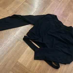 Svart långärmad topp från Aimo - Säljer en svart långärmad topp från JX. Toppen har en stilren design med en croppad passform och är tillverkad i ett mjukt material. Perfekt för en trendig look. tränings tröja. Kan även användas som L