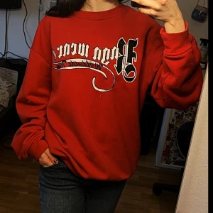Röd sweatshirt - Säljer en cool röd sweatshirt med tryck i svart och vitt på framsidan. Tröjan har en avslappnad passform och långa ärmar, perfekt för en casual look. Den är gjord i mjukt material för extra komfort.