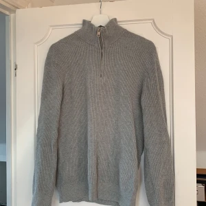 Grå stickad tröja  - Säljer en stilren grå stickad tröja från H&M i slim fit. Tröjan har en dragkedja vid halsen och långa ärmar, perfekt för kyligare dagar. Den ribbade strukturen ger en snygg och modern look. Passar bra till både jeans och chinos. Skick 9/10