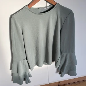 Grön tröja med volangärmar - Säljer en grön tröja med volangärmar i storlek S, varan är lite nooprig här och där.