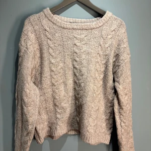 Beige stickad tröja från 157 - Mysig beige stickad tröja från 157 med flätmönster. Perfekt för kyliga dagar med sin varma och bekväma design. Tröjan har långa ärmar och en rund halsringning.