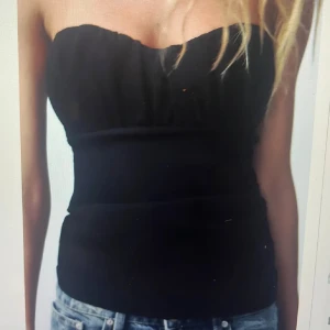 Svart tubtopp - Snygg svart tubtopp som passar perfekt till jeans eller kjol. Den är axelbandslös och har en enkel design som gör den lätt att matcha med olika stilar.