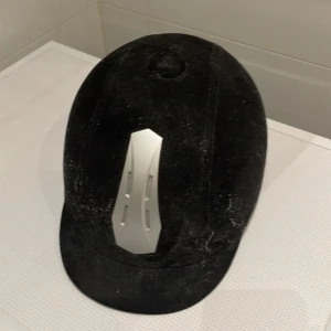 Svart ridhjälm från CRW - Jag säljer en stilren svart ridhjälm från CRW med en elegant silverdetalj framtill. Hjälmen har en justerbar rem för perfekt passform och den är justerbar där bak och är designad för ridning. Perfekt för den stilmedvetna ryttaren. Lite dammig för att den har legat i en låda men ryttare vet ju hur hjälmen blir😉