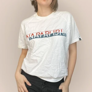 Vit t-shirt från Napapijri - Säljer en vit t-shirt från Napapijri med tryck i rött och blått på bröstet. Jag på bilden har strl 36 på överdelar och är 170cm. Klicka på köp nu <3