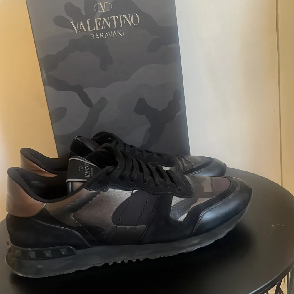 Snygga Valentino Garavani sneakers i svart och silver med ett coolt camouflage-mönster. Dustbag och box finns. Skorna har snörning och är tillverkade i skinn och syntet. Perfekta för att ge din outfit en lyxig touch. Fråga om det är något!. Kengät.