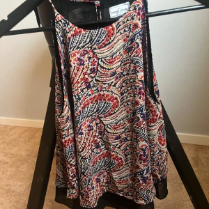 Mönstrad linnetopp från Crocker Apparel - Säljer en färgglad och mönstrad linnetopp från Crocker Apparel. Toppen har ett livligt mönster i rött, blått och beige med svarta detaljer. Perfekt för en somrig look!