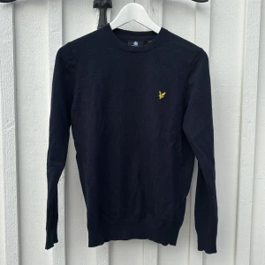 Mörkblå  tröja från Lyle & Scott - Säljer en stilren mörkblå tröja från Lyle & Scott med deras ikoniska gula logotyp på bröstet. Tröjan har långa ärmar och en rund halsringning, perfekt för en klassisk look. Säljes i mycket bra begagnat skick. 9/10 nypris 899kr på MQ