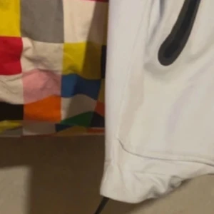 Vit vindjacka från Under Armour - Säljer en stilren vit vindjacka från Under Armour med huva och svarta dragkedjor. Jackan har en sportig look och är perfekt för blåsiga dagar. Den har justerbara snören vid huvan för extra skydd.