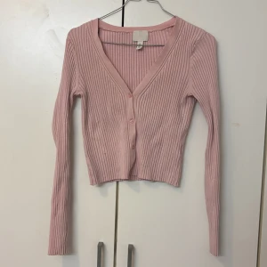 Rosa, vitt och mörk rosa ribbad kofta - Säljer en söt rosa ribbad kofta med v-ringning och knappar framtill. Den är croppad och har långa ärmar, perfekt för en stilren look.