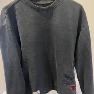 Mörkblå sweatshirt med broderad detalj - Snygg svart sweatshirt från Vetements med en unik broderad detalj i form av en hand på baksidan. Tröjan har långa ärmar och en rund halsringning. Perfekt för en stilren och avslappnad look.