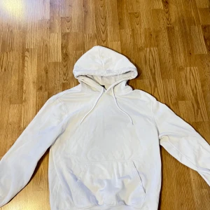 Vit hoodie från H&M - Säljer en vit hoodie från H&M i relaxed fit. Den har en klassisk design med en stor ficka framtill och justerbar huva. Perfekt för en avslappnad stil.