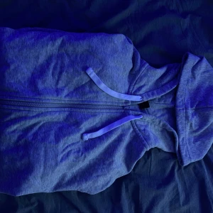 Grå huvtröja med dragkedja - Säljer en blå huvtröja med dragkedja framtill. Tröjan har långa ärmar och en praktisk huva med snören. Perfekt för en avslappnad stil. Nypris 350kr