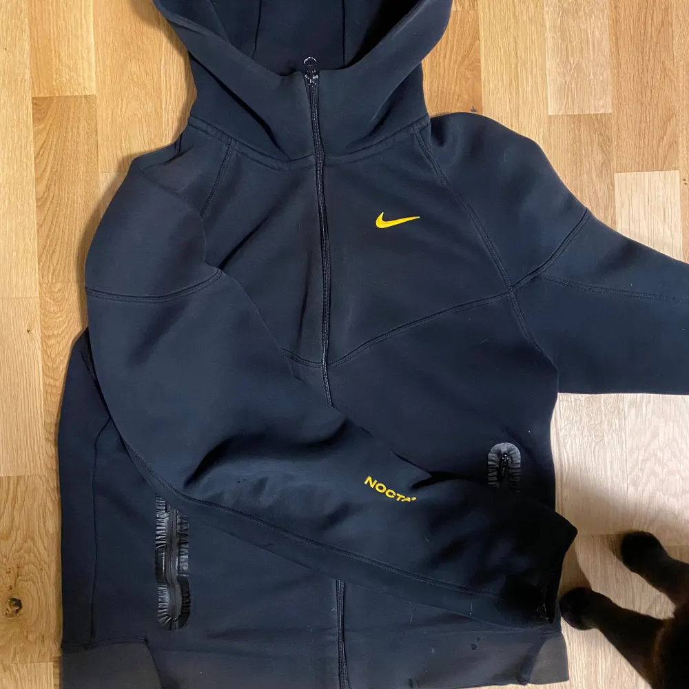 Säljer en svart hoodie från Nike med gul logga på bröstet. Den har en dragkedja framtill och en praktisk huva. Perfekt för en sportig look eller avslappnade dagar. 🖤. Hupparit & Collegepaidat.