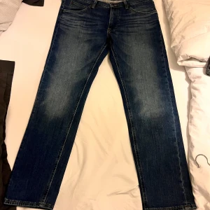 Blå jeans från Lee - Snygga blå jeans från Lee med klassisk femficksdesign och dragkedja. De har en straight passform och är perfekta för en avslappnad stil. Märkeslogga på baksidan ger en extra touch.