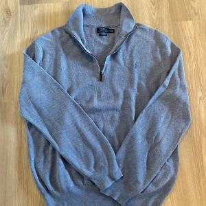 Blå polo Ralph lauren half zip - Säljer en stilren grå tröja från Polo Ralph Lauren i Pima bomull. Tröjan har en halv dragkedja och ett broderat logotypmärke på bröstet. Perfekt för en avslappnad och snygg look. Dragkedjan är lite trög men funkar med lite kraft.