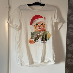 Vit t-shirt med julmotiv från Mywear - Vit t-shirt från Mywear med ett gulligt julmotiv av en katt i tomteluva. Perfekt för att sprida julstämning! Kortärmad och tillverkad i mjukt material.