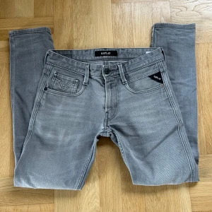 Grå jeans från Replay - Snygga grå jeans från Replay i modellen Anbass. Snygg ljusgrå färg som passar till allt. Storleken är W29 och L32 men dem har krymt lite i tvätten så nu sitter dem som W28 och L30. Passformen är slim fit. Dem har en liten defekt vid vänster ben men det är inte så synligt, mycket bra skick annars.