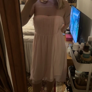 Ljusrosa axelbandslös klänning från Vila  - Säljer en söt ljusrosa axelbandslös klänning med smockdetaljer i ryggen. Klänningen har en luftig passform och är perfekt för varma dagar. Den är knälång och har en mjuk🌴☀️Perfekr inför sommaren🥰 Står st M men jag tycker den passar mig som har S 