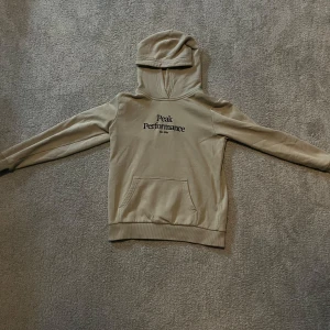 Beige hoodie från Peak Performance - Säljer en stilren beige hoodie från Peak Performance. Den har en klassisk design med en känguruficka framtill och en bekväm huva. Perfekt för en avslappnad stil.