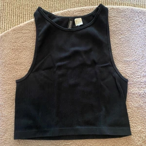 Tröja - Snygg svart ribbad topp/linne från H&M Divided. Perfekt för en casual look med sin croppade design och ärmlösa stil. Enkel att matcha med olika outfits.😻Perfekt att ha på en varm sommardag eller som basplagg när som❤️