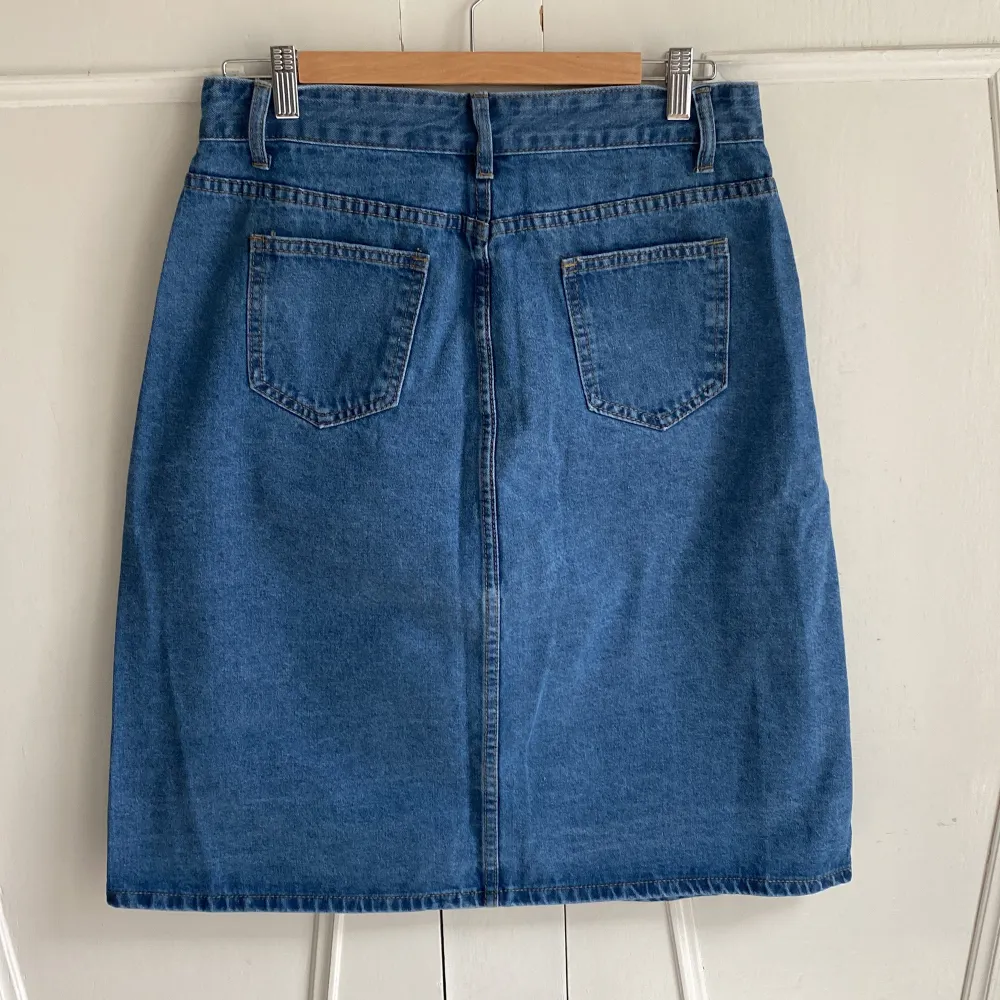 Snygg blå jeanskjol med knappar hela vägen fram och praktiska fickor både fram och bak. Kjolen har en klassisk design med bälteshällor i en denim utan stretch. Passar bra till en enkel t-shirt eller en stickad tröja. Midja 79 cm, längd 62. Står storlek L men är nog snarare S/XS. Aldrig använd. . Hameet.