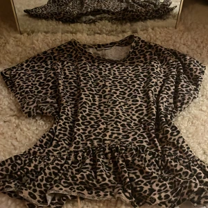 Leopardmönstrad topp från Kappahl - Säljer en leopardmönstrad topp från Kappahl med korta ärmar och volangdetalj vid nederkanten. Perfekt för att ge en vild touch till din outfit. 🐆