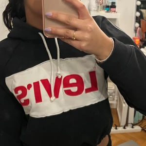 Vintage hoodie från Levi's - Säljer en svart hoodie från Levi's med en stor röd logga på bröstet. Hoodien har en justerbar dragsko i midjan och vita snören vid huvan. Perfekt för en casual look! 🖤