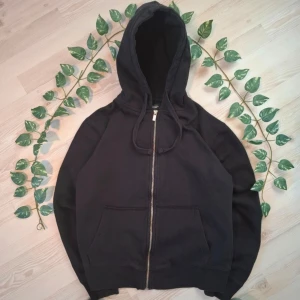 Svart huvtröja från lager 157 - Säljer en svart huvtröja med dragkedja från lager 157. Tröjan har en klassisk design med huva och snörning samt ribbade muddar vid ärmslut och nederkant. Perfekt för en avslappnad stil.