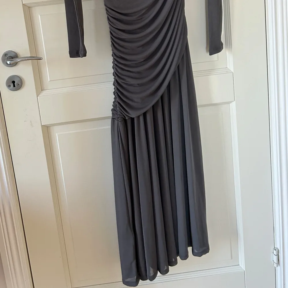 Elegant grå långklänning från H&M med draperad design som ger en snygg siluett. Klänningen har långa ärmar och är perfekt för en stilren look. Materialet är mjukt och följsamt, vilket gör den bekväm att bära. Perfekt för speciella tillfällen eller en kväll ute.. Mekot.