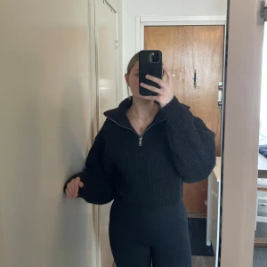 Svart stickad tröja från Gina Tricot - Säljer en svart stickad tröja från Gina Tricot med dragkedja framtill. Tröjan har en hög krage och långa ärmar, perfekt för kyligare dagar. Den är både stilren och bekväm.