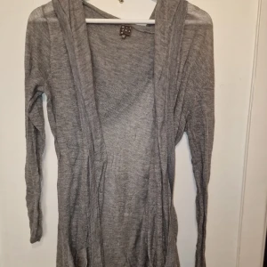 Grå kofta från Rituals - Säljer en stilren grå kofta från Rituals. Den har en luva och långa ärmar, perfekt för en avslappnad look. Garderobsrensning så kika gärna på övriga auktioner.