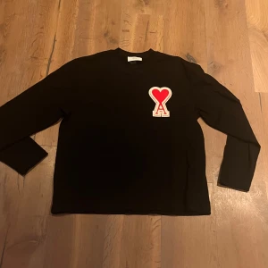 Svart tröja från Ami Alexandre Mattiussi - Snygg svart tröja från Ami Alexandre Mattiussi med ett rött hjärta på bröstet. Tröjan har långa ärmar och en klassisk passform. Perfekt för en stilren look.