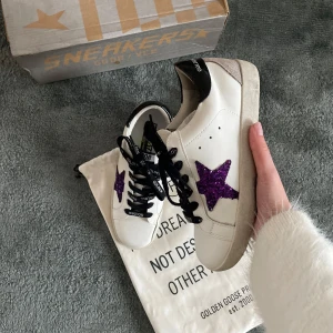 Golden Goose skor - Säljer nu ett par snygga vita sneakers från Golden Goose med en glittrig lila stjärna på sidan. Skorna är i riktigt bra skick och är i storlek 38. Vid frågar och funderingar är det bara att höra av sig☺️