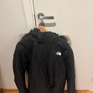 Svart vinterjacka från The North Face - Säljer en svart vinterjacka från The North Face med pälskantad huva. Jackan har dragkedja och är tillverkad i polyester och nylon. Perfekt för kalla dagar. Jackan är 2-3 år gammal och använd 2-3 gånger