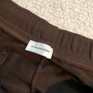 Bruna mjukisbyxor från By Malene Birger - Säljer dessa snygga bruna mjukisbyxor från By Malene Birger med bekväm resårmidja och snörning. Perfekta för en avslappnad stil. Tillverkade i mjukt material för extra komfort. Killmodel 
