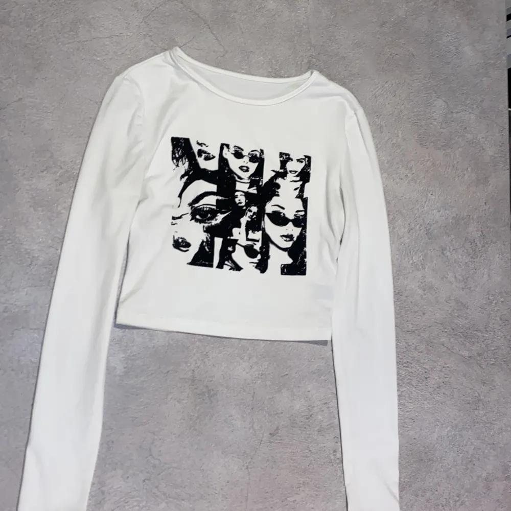 Snygg vit långärmad croppad topp med ett coolt svart tryck av ansikten. Perfekt för att ge din outfit en edgy touch. Tillverkad i ett mjukt och bekvämt material.. Yläosat.
