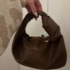 Brun flätad handväska - Säljer en snygg brun handväska med flätat mönster och guldig dragkedja. Aldrig använd 🤎 