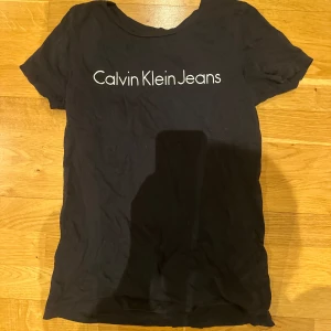 Svart t-shirt från Calvin Klein Jeans - Snygg svart t-shirt från Calvin Klein Jeans med vit logga på bröstet. Perfekt för en stilren och avslappnad look. Kortärmad och i mjukt material för bekväm passform.