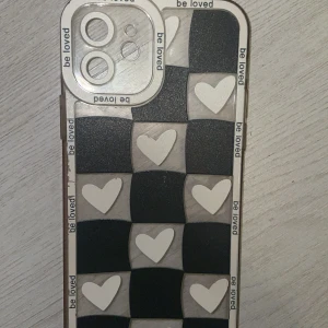 Svart vitt Mobilskal med hjärtmönster - Snyggt mobilskal med ett schackrutigt mönster i svart och vitt, dekorerat med hjärtan och texten 'be loved'. Skalet har en transparent kant och är designat för att skydda kameran. Perfekt för att ge din mobil en personlig touch! Endast använd typ 2 gånger och fick i present. Säljer då jag ska byta telefon📱 och inte längre har användning för den. Pris kan diskuteras!! Jag står inte för postens slarv