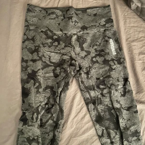 Gråa camo leggings från Gymshark  - Snygga camo-mönstrade leggings från Gymshark i grå och svart. De är högmidjade och har en tight passform, perfekta för träning. Materialet är stretchigt och bekvämt.