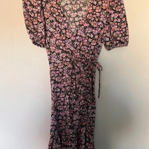 Blommig omlottklänning - Söt blommig omlottklänning i rosa och svart med korta ärmar och knytband i midjan. 