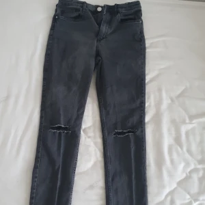 Svarta skinny jeans - Snygga svarta skinny jeans med hög midja och slitna detaljer vid knäna. Perfekta för en trendig look. Tillverkade i denim för en klassisk känsla.