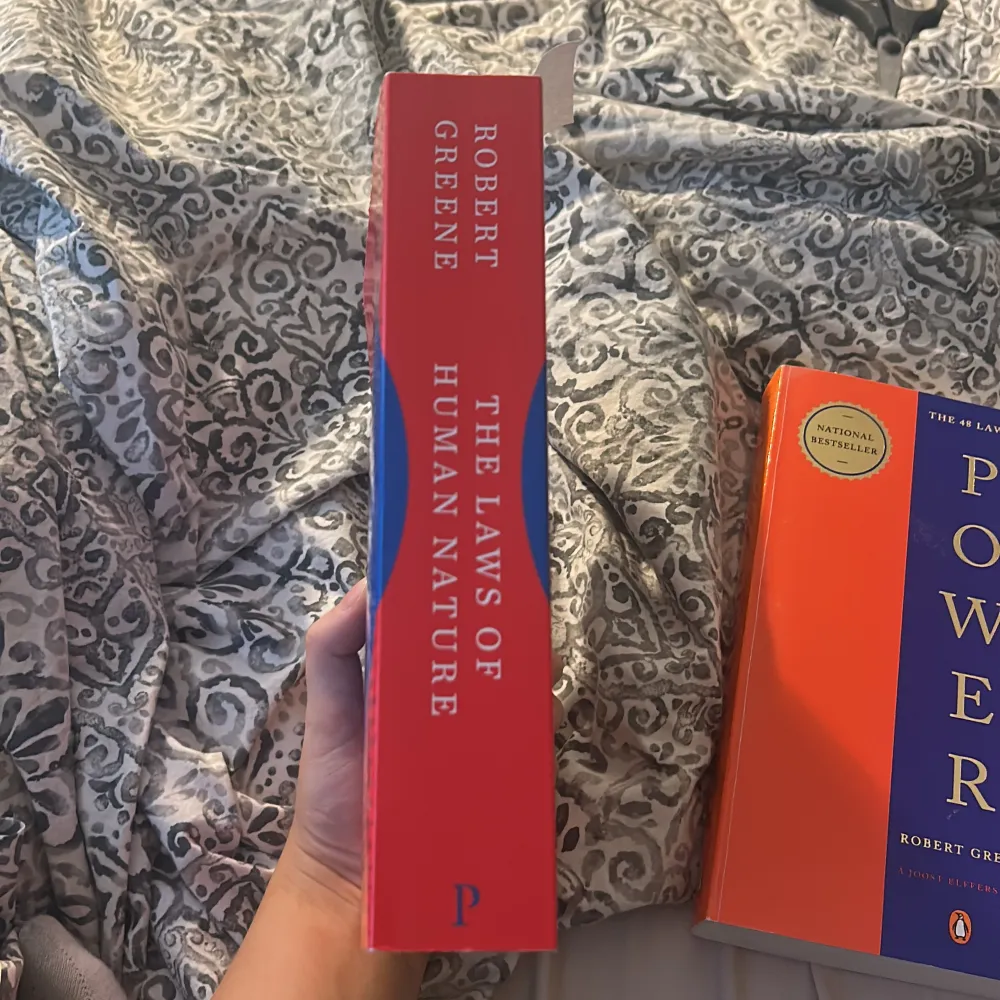 Säljer boken 'The Laws of Human Nature' av Robert Greene. Den har en röd och blå omslag med titeln i stora vita bokstäver. Perfekt för den som vill förstå mänskligt beteende och psykologi. Boken är en national bestseller och erbjuder insikter i hur man kan tolka och påverka andra.. Böcker.