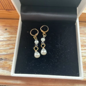 Long pearl  - Eleganta guldörhängen med hängande pärlor. Perfekta för att ge en sofistikerad touch till din stil. De har en enkel och stilren design med små ringar och två pärlor i varje örhänge. Har inte använts. Helt nygjorda och handgjorda. Inte säker på om de är nickelfritt.