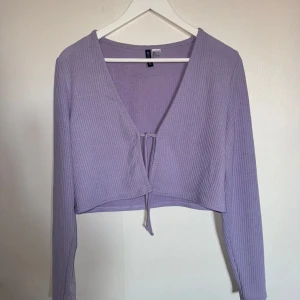 Lila ribbad kofta från H&M - Säljer en lila ribbad kofta från H&M med knytning framtill. Koftan har en v-ringad design och långa ärmar, perfekt för lager-på-lager stil. Passar utmärkt till både jeans och kjol. 💜