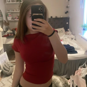 Röd rygglös topp - Säljer en snygg röd rygglös topp med korta ärmar. Perfekt för en trendig look. Toppen har en tight passform och är gjord i ett mjukt polyester material.